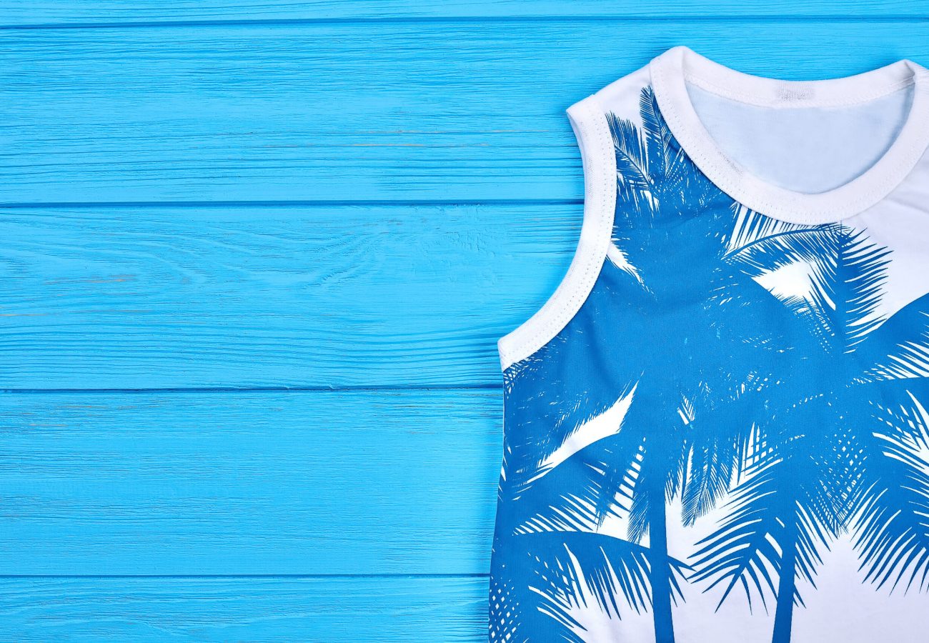 Childrens sleeveless fashionable t-shirt. Childrens sleeveless fashionable t-shirt. White printed t-shirt for child and copy space. Childrens summer garment, blue wooden background.