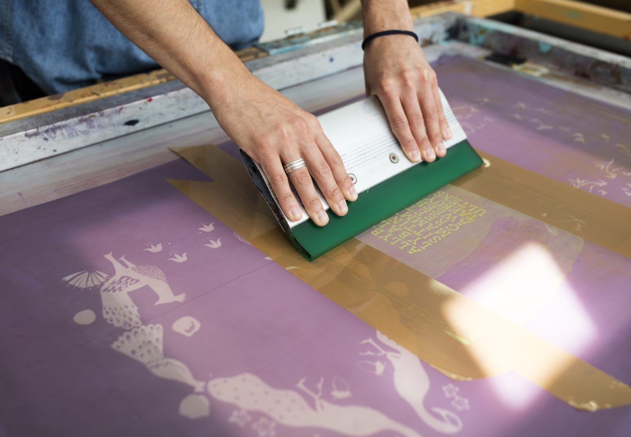 Hands of young male printer using squeegee in printing press studio Hands of young male printer using squeegee in printing press studio